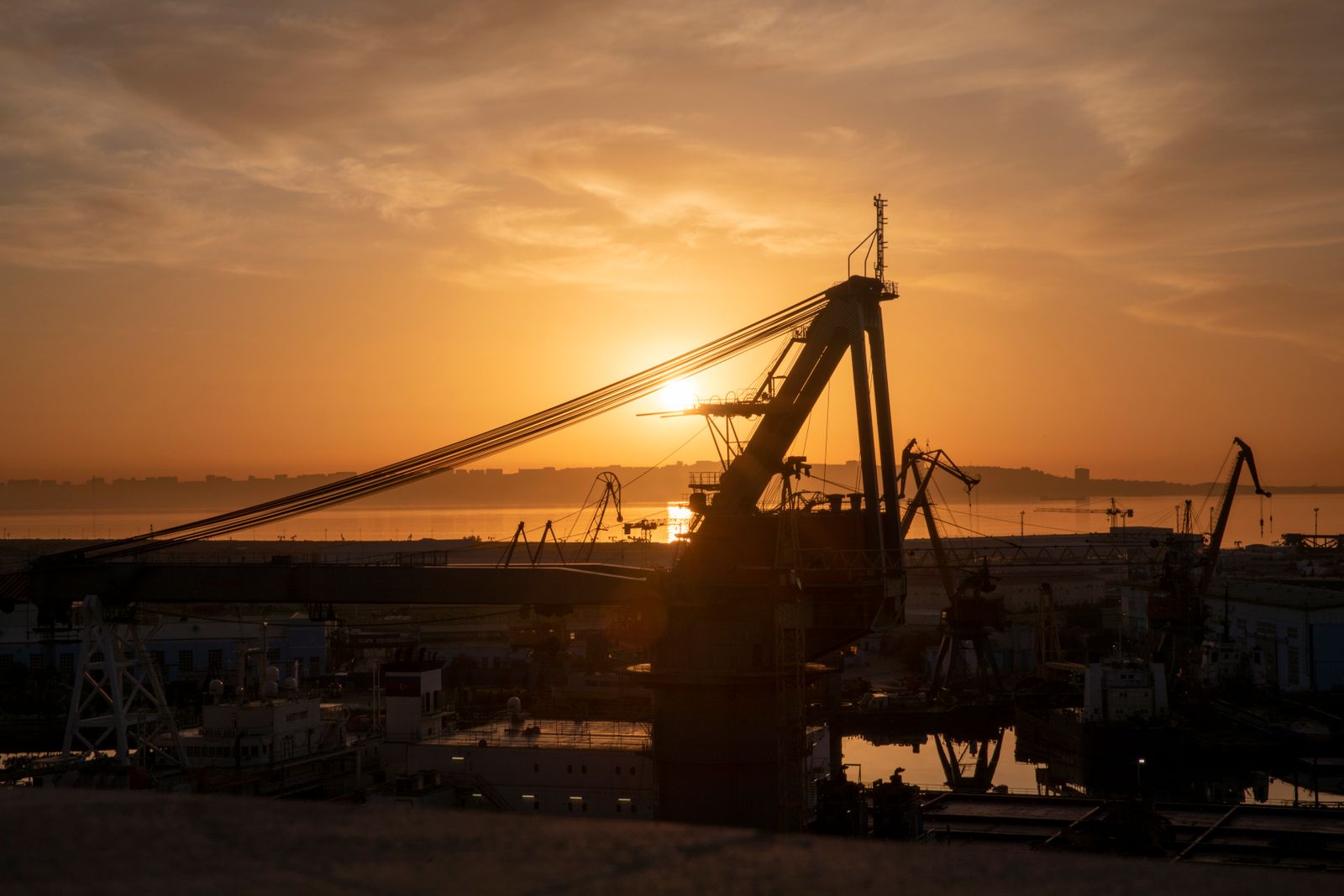 Harbour crane silhouetted against a low sun over a working port