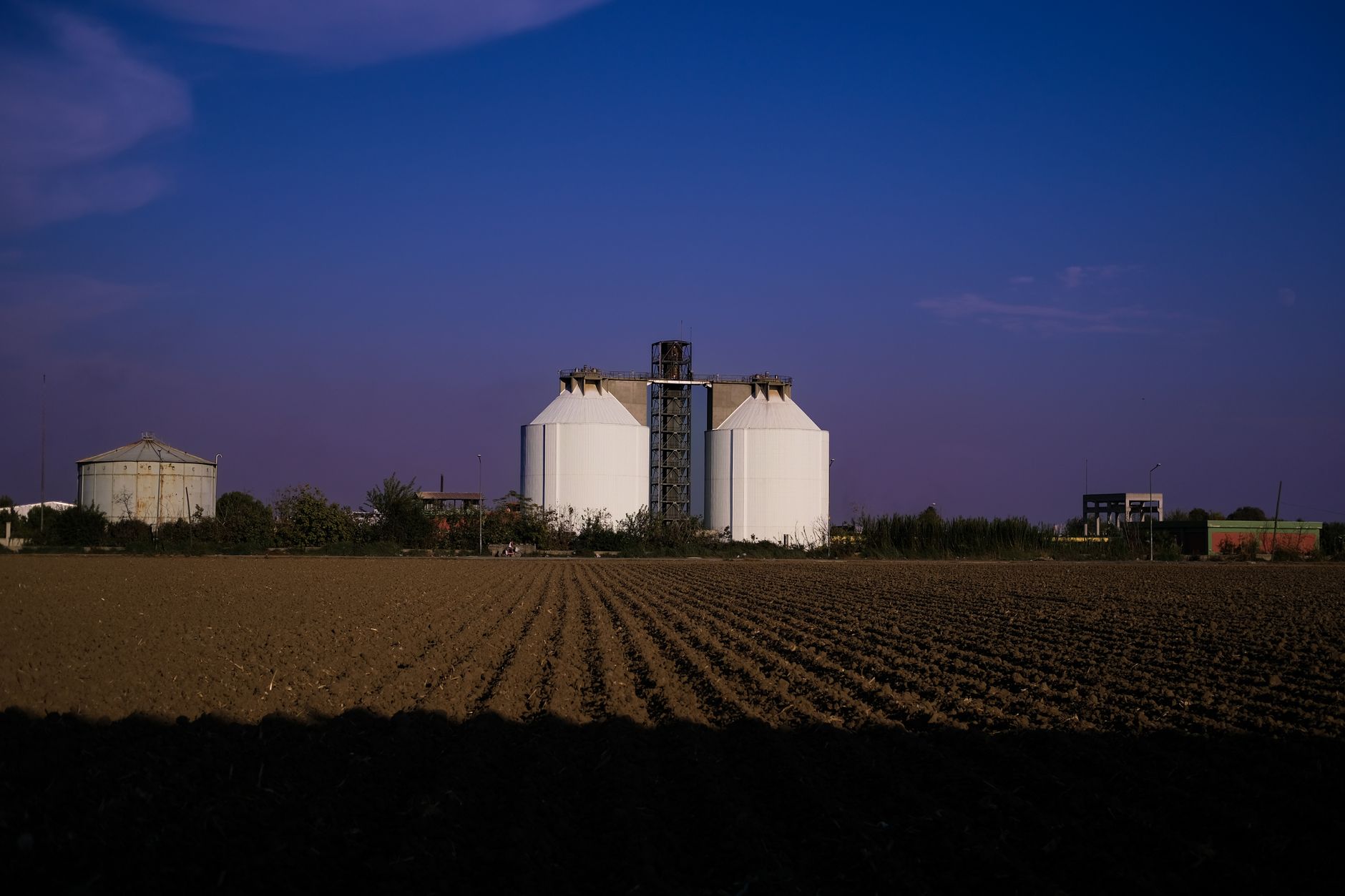 Grain silos at dusk behind a ploughed field