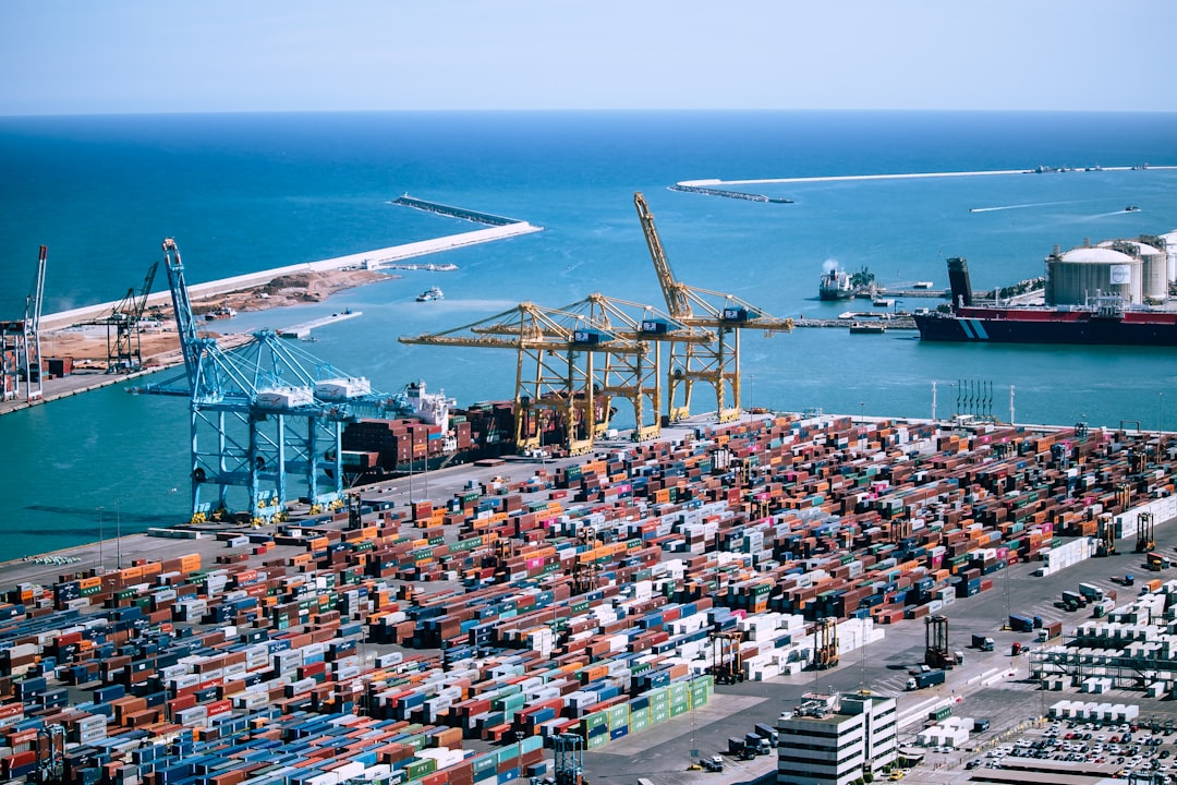 Mediterranean container port with quay cranes, stacked boxes and a breakwater beyond