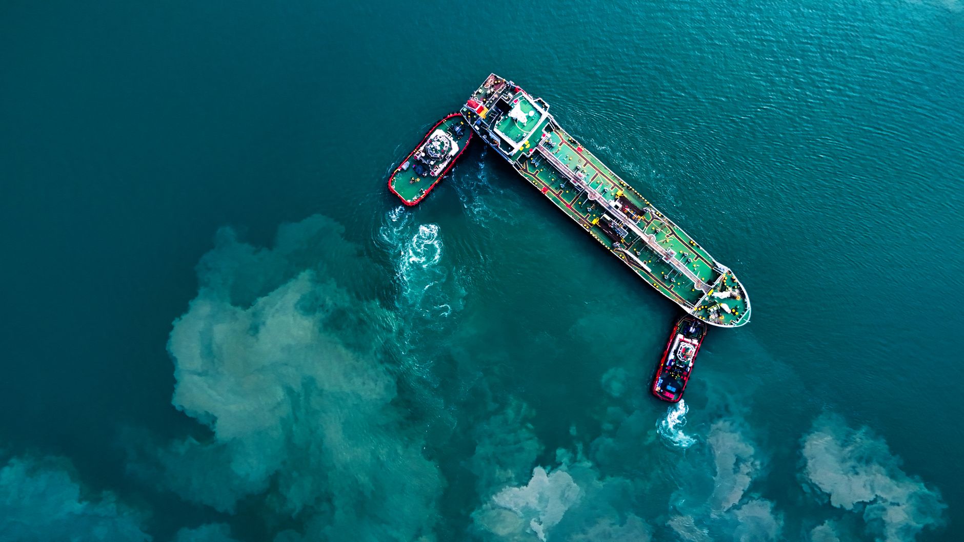 Overhead view of a tanker under escort by two tugs in open water