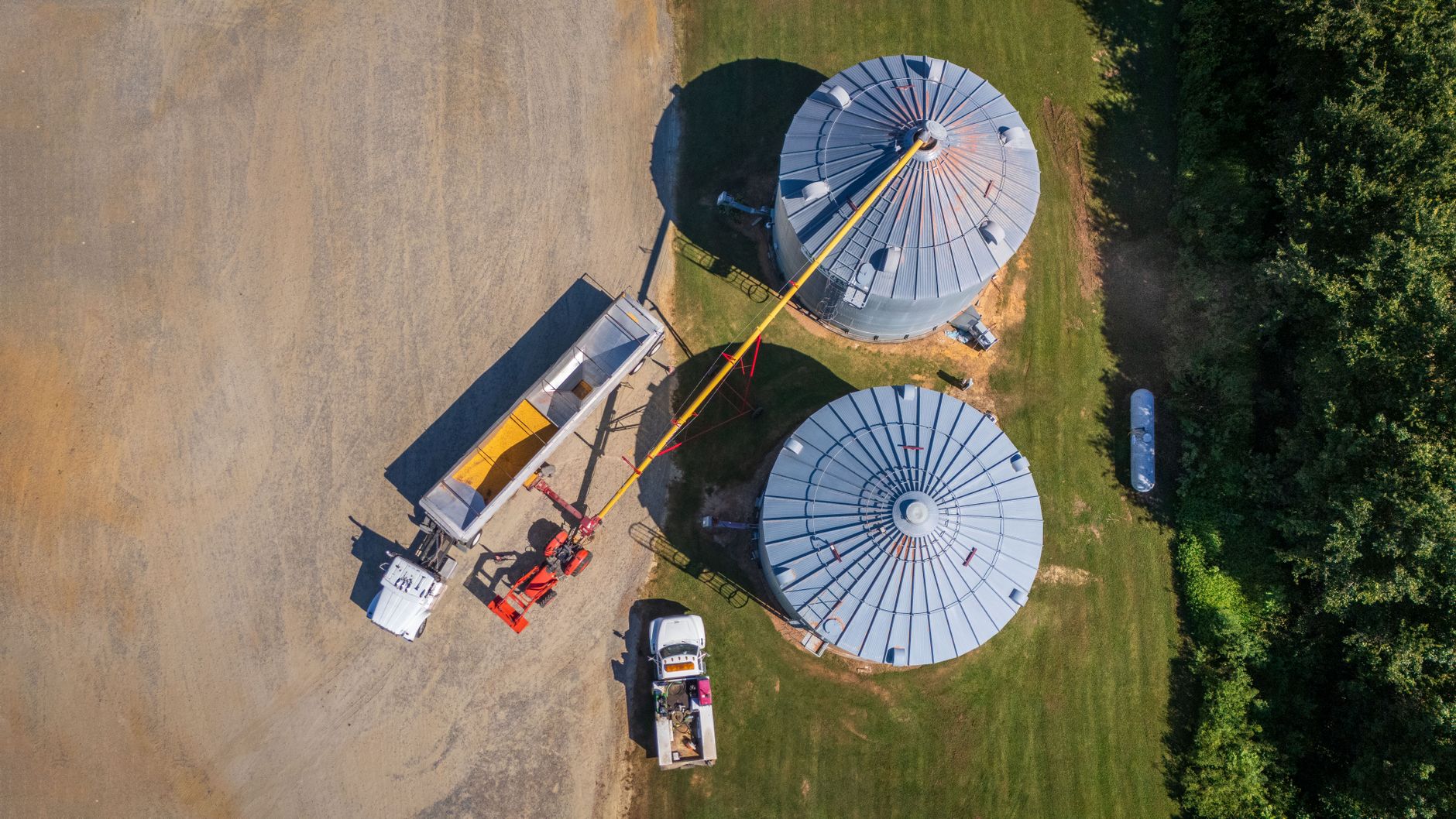 Aerial view of grain storage silos with a hopper truck being loaded at a farm