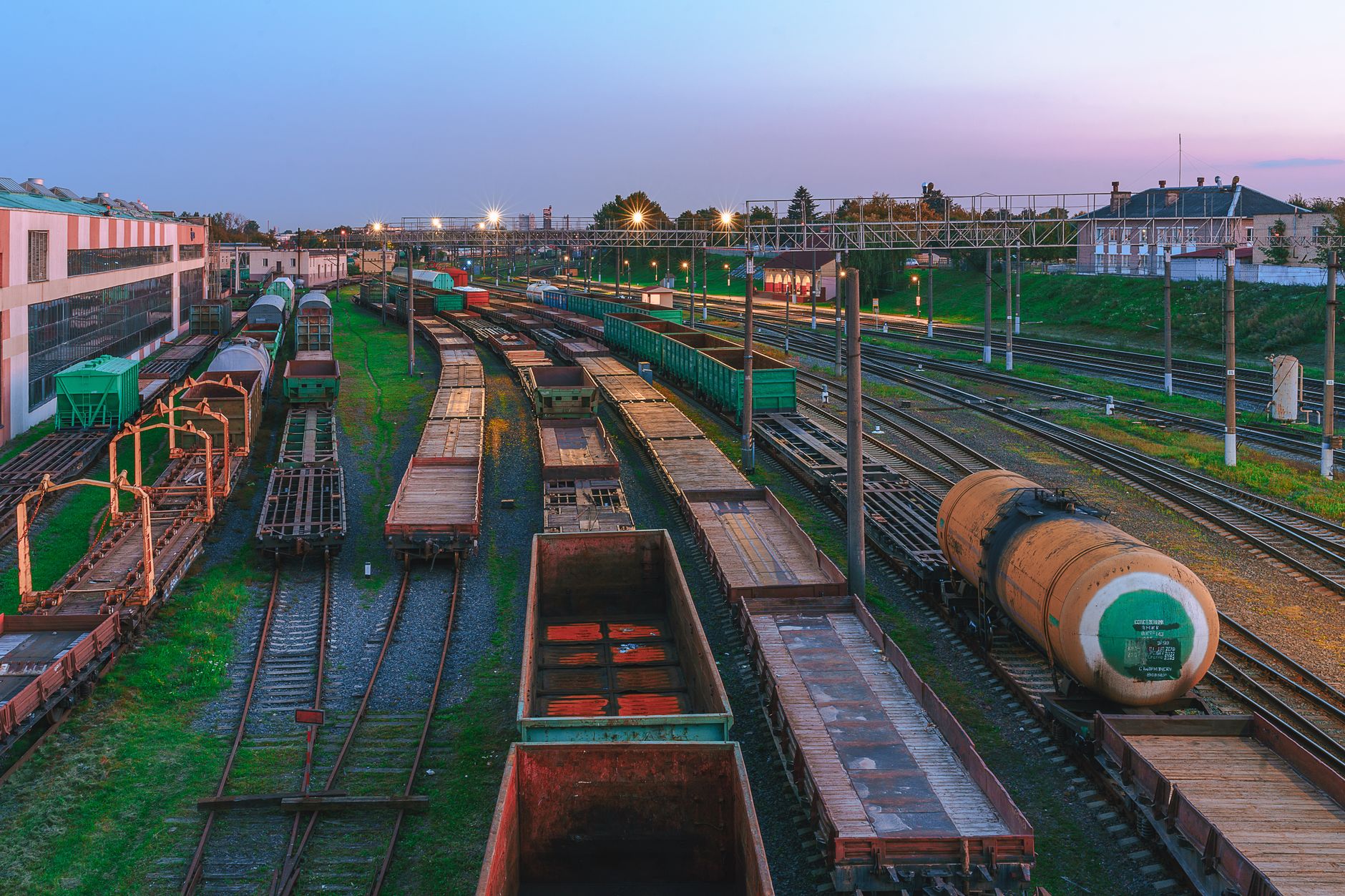 Broad-gauge yard at dusk with flat wagons, open wagons and a tank car standing on adjacent roads