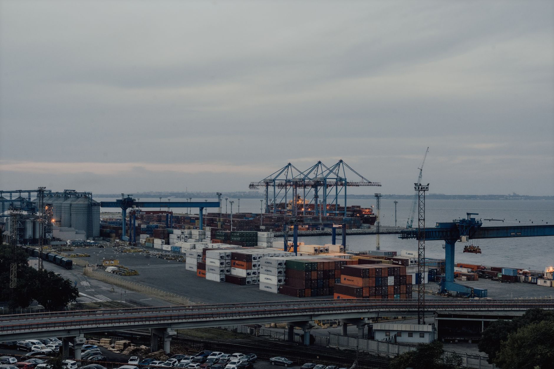 Gateway port at dusk with grain silos, quay cranes and a rail viaduct behind the yard