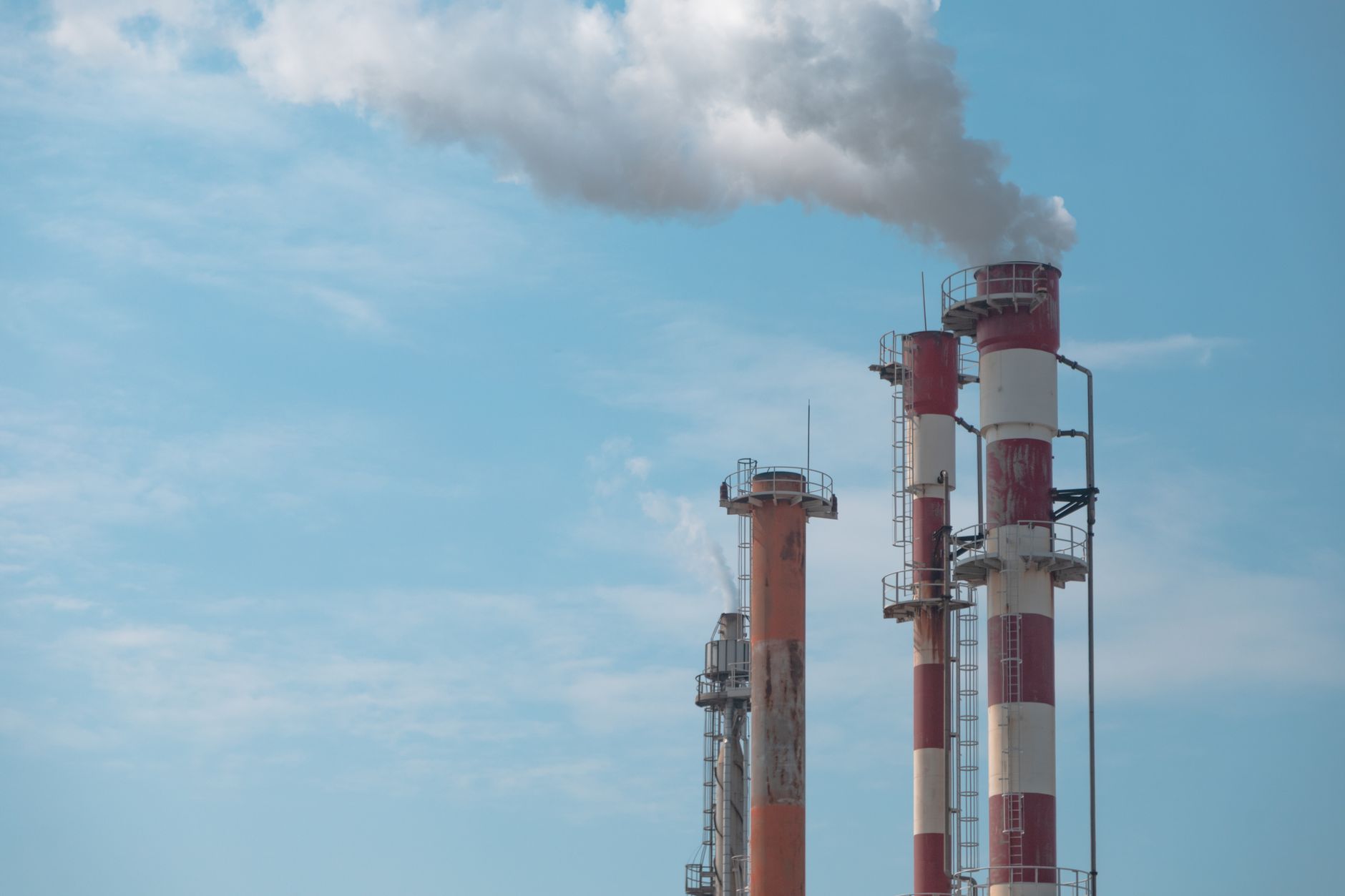 Industrial smokestacks emitting a plume against a blue sky