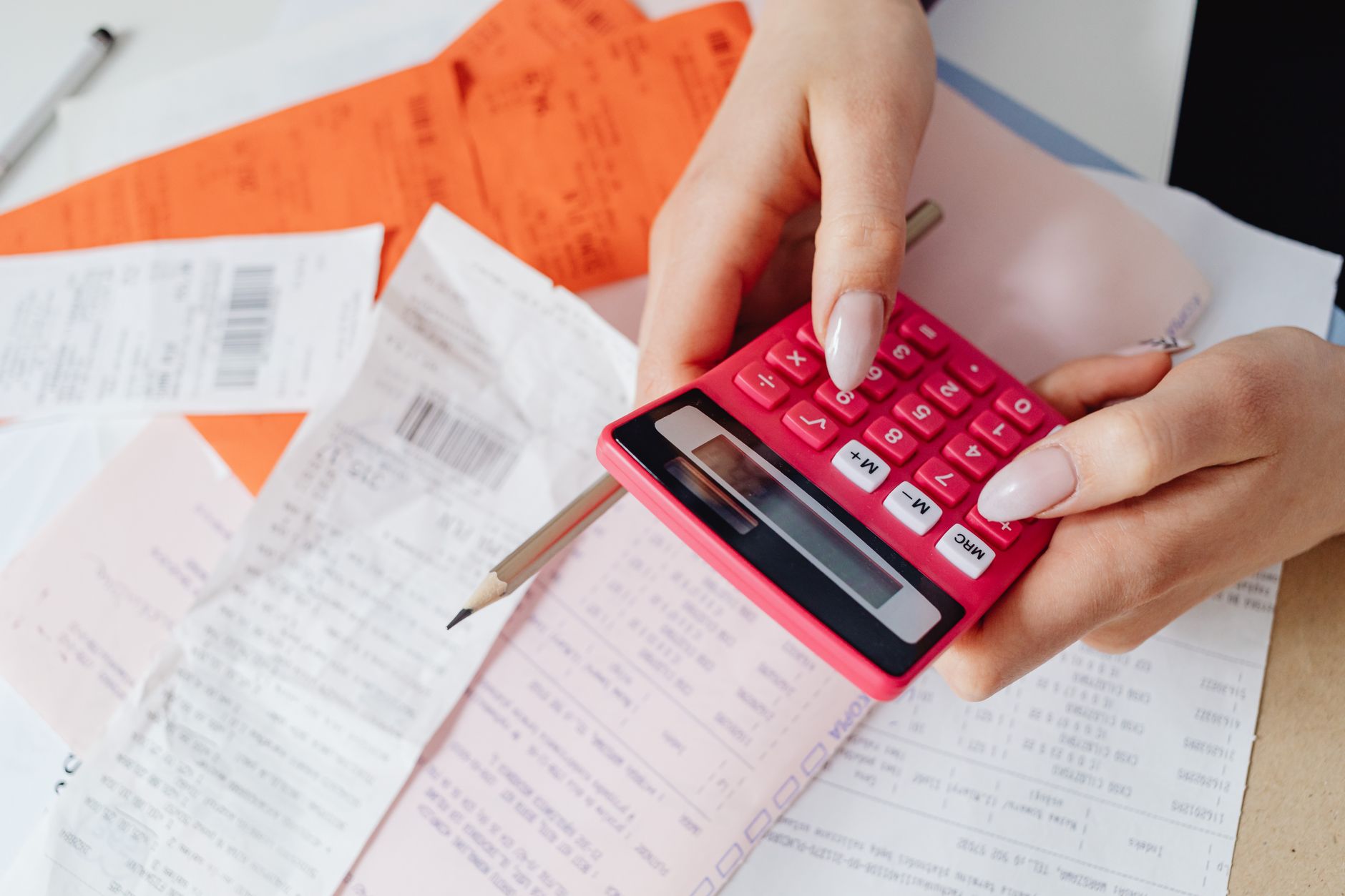 Hands checking invoice totals on a calculator over printed receipts