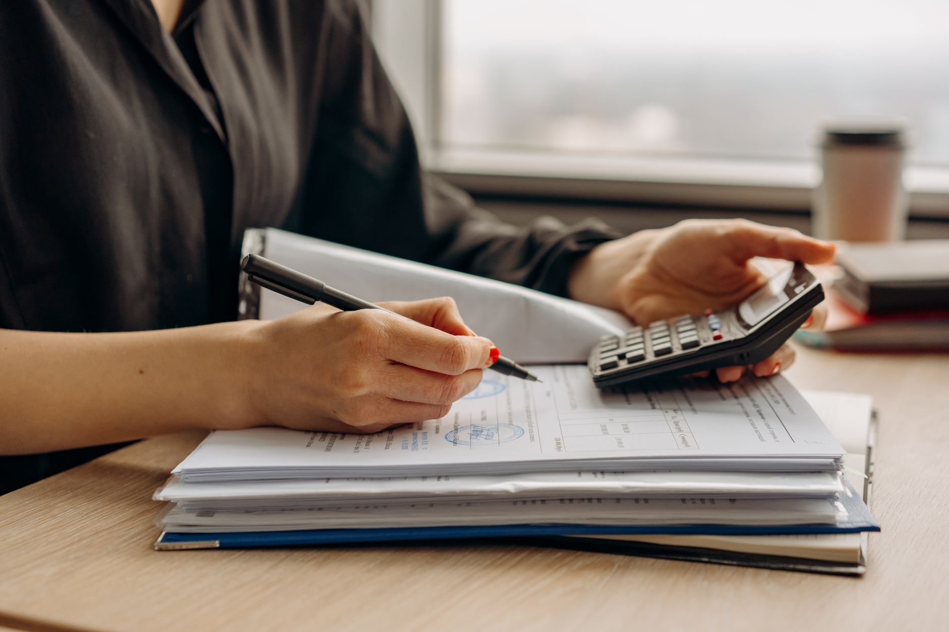 Hands with calculator over stamped customs invoices, calculating import duty under the First Sale Rule