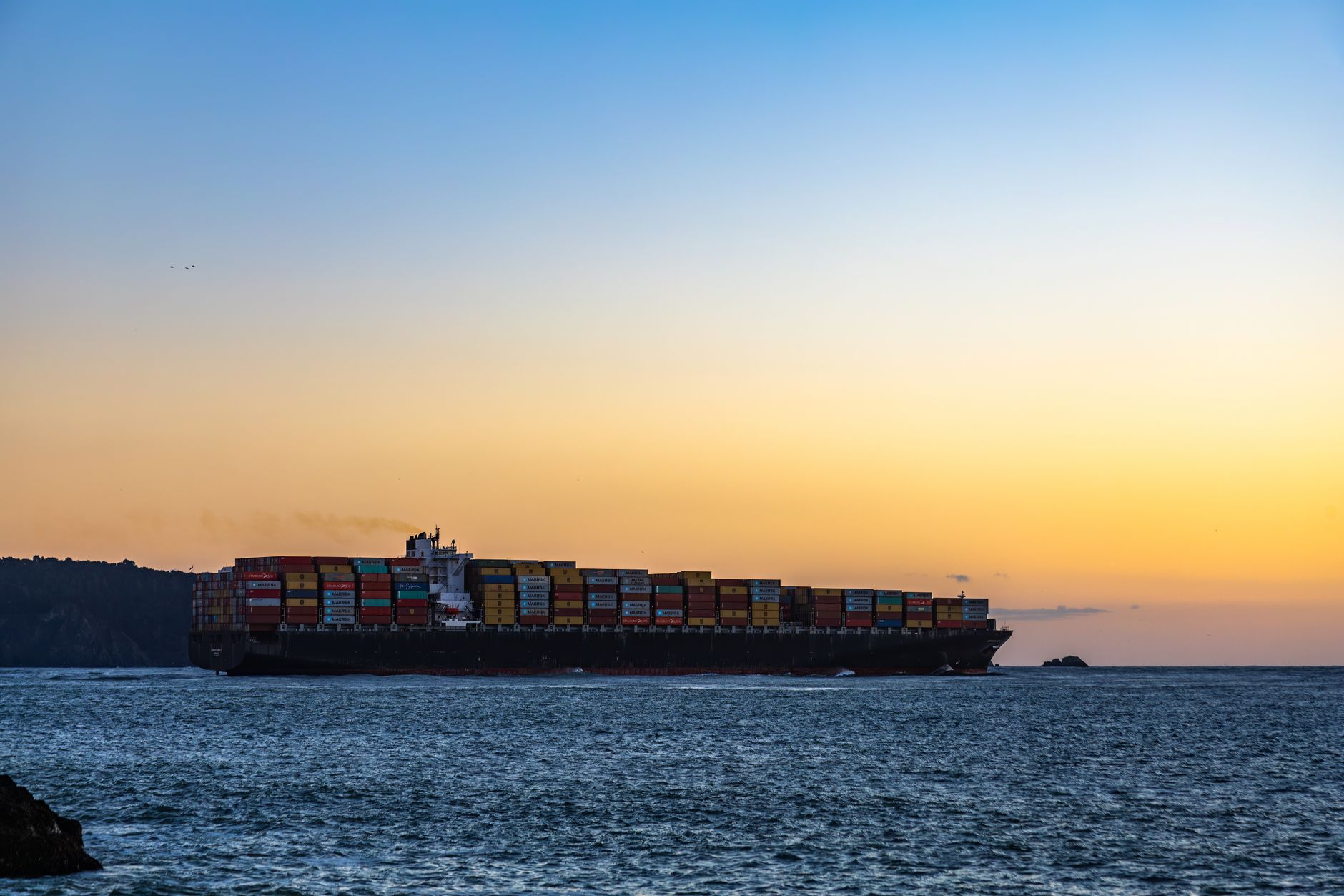 Container ship at sea with exhaust plume at sunset