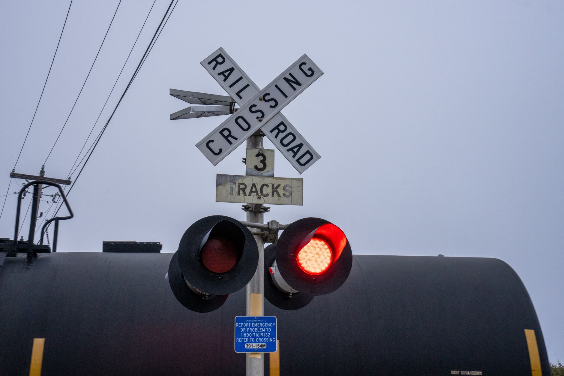 Level crossing signal showing red as a tank car passes behind the crossbuck