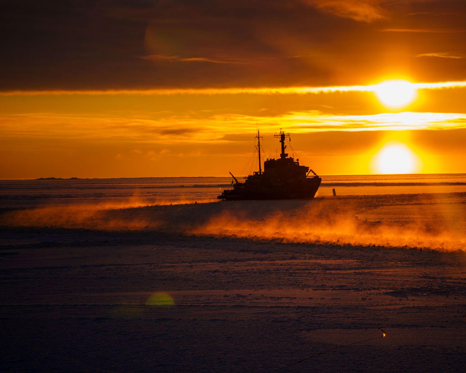 Icebreaker silhouetted at sunset while working through a field of pack ice